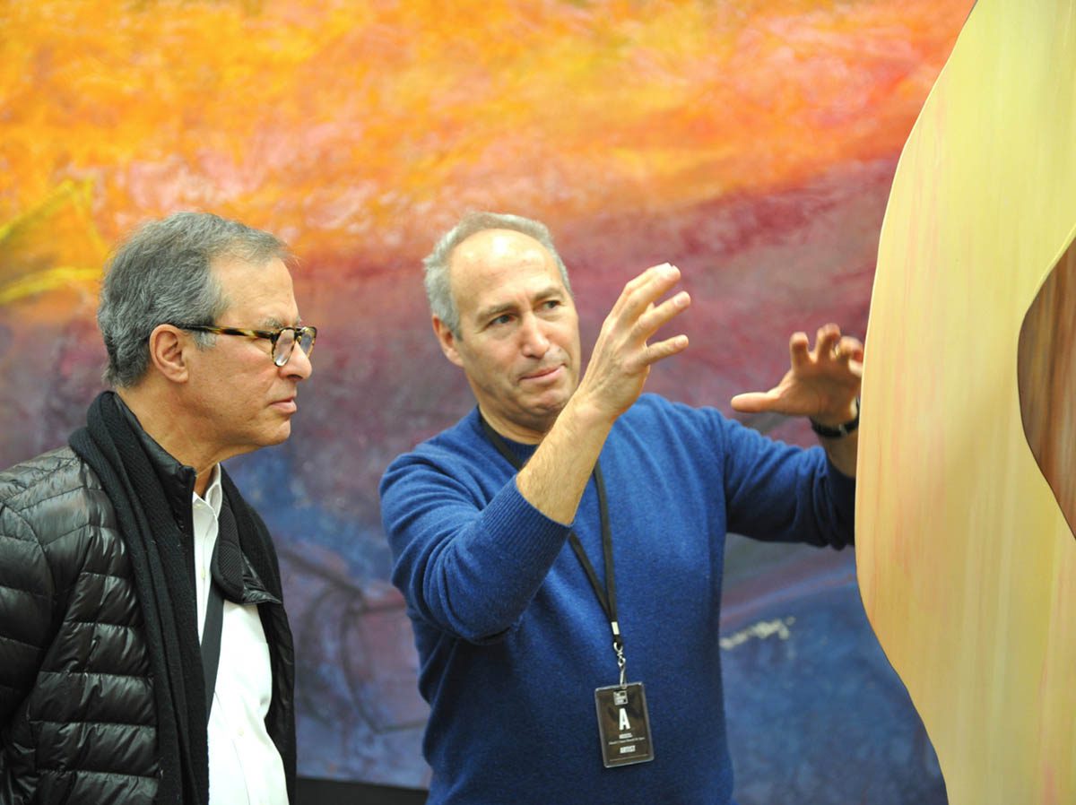 Two men are looking at a painting in the background.