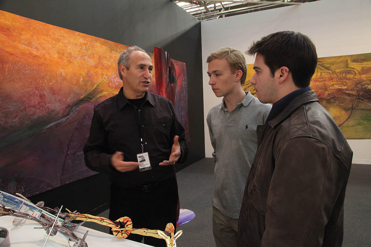 Three men are talking in front of a painting.